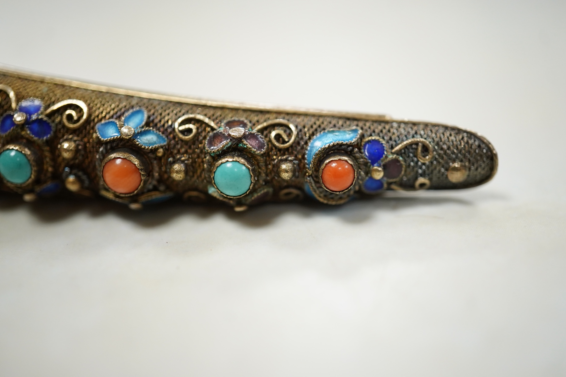 A Chinese silver gilt coral and turquoise nail guard brooch, composed of filigree, set with coral and turquoise cabochons, applied with foliate designs in blue enamel, length 8.4cm, stamped SILVER, Condition: in good con